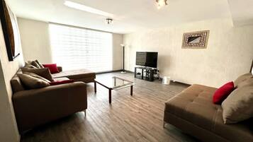 A spacious living room with two sofas, a coffee table, and a flat-screen TV on a stand.