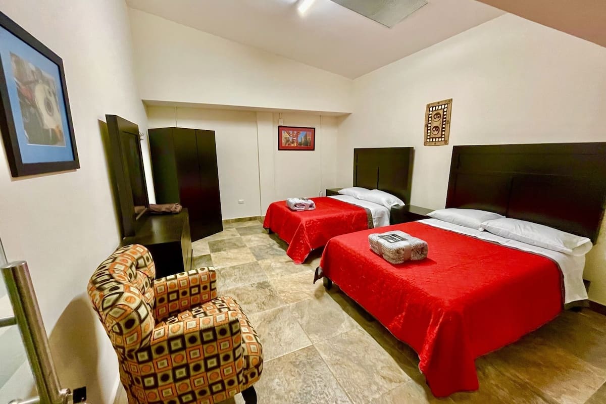 Une chambre d’hôtel avec deux lits, une chaise, un téléviseur et une horloge au mur.