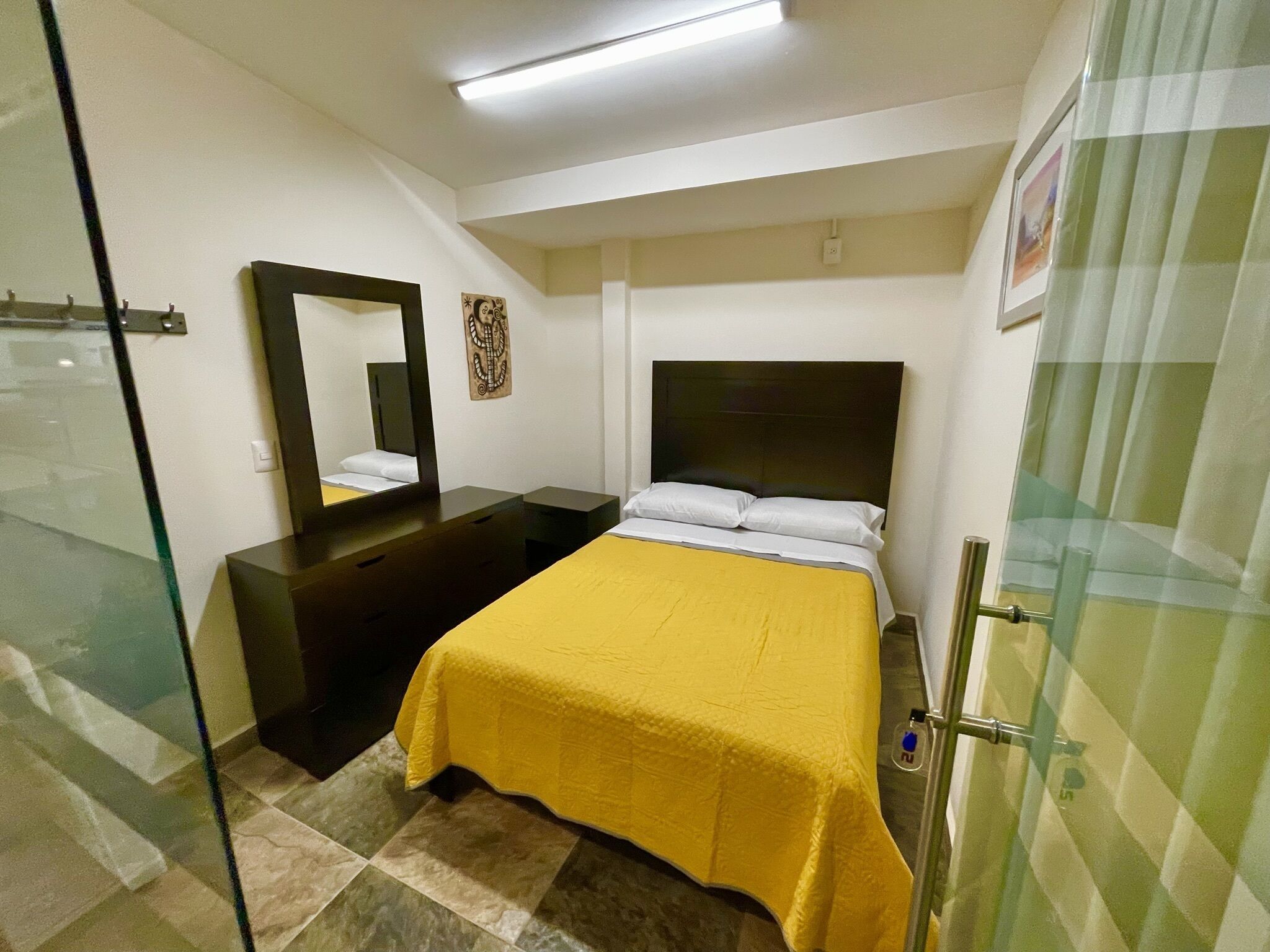 A hotel room with a bed, a dresser, a mirror, and a shower area.
