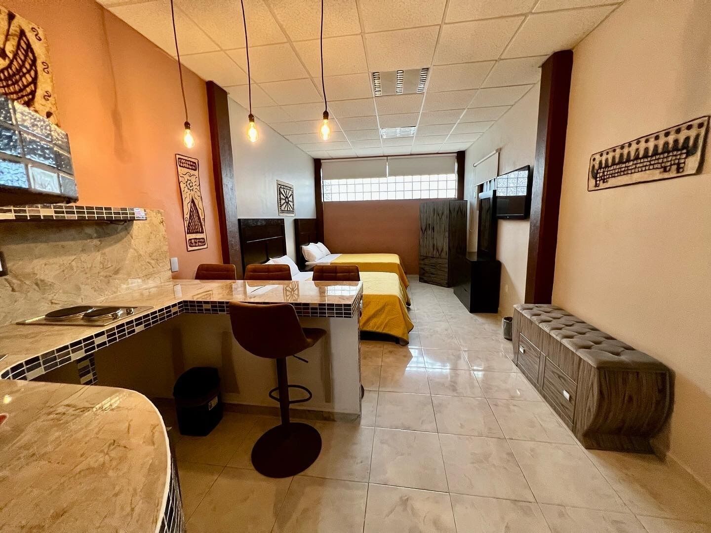 Habitación de hotel con kitchenette, zona de comedor, dos camas, televisor y un ventanal grande.