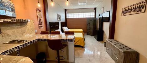 Habitación de hotel con kitchenette, zona de comedor, dos camas, televisor y un ventanal grande.