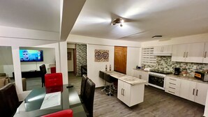 A modern kitchen with white cabinets, a dining area with red chairs, and a TV displaying a movie. - Downtown Treasure Place (Mexico City)