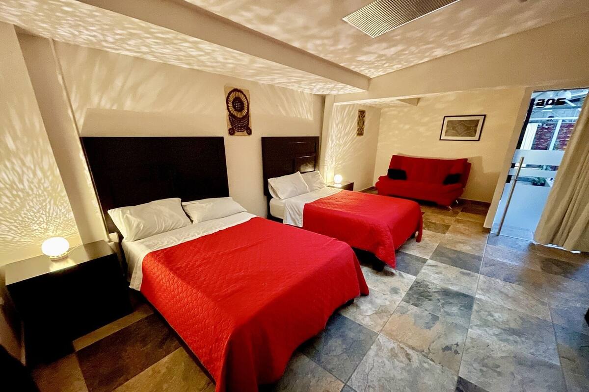 Une chambre d’hôtel avec deux lits, une table de chevet, une chaise rouge et une petite table.