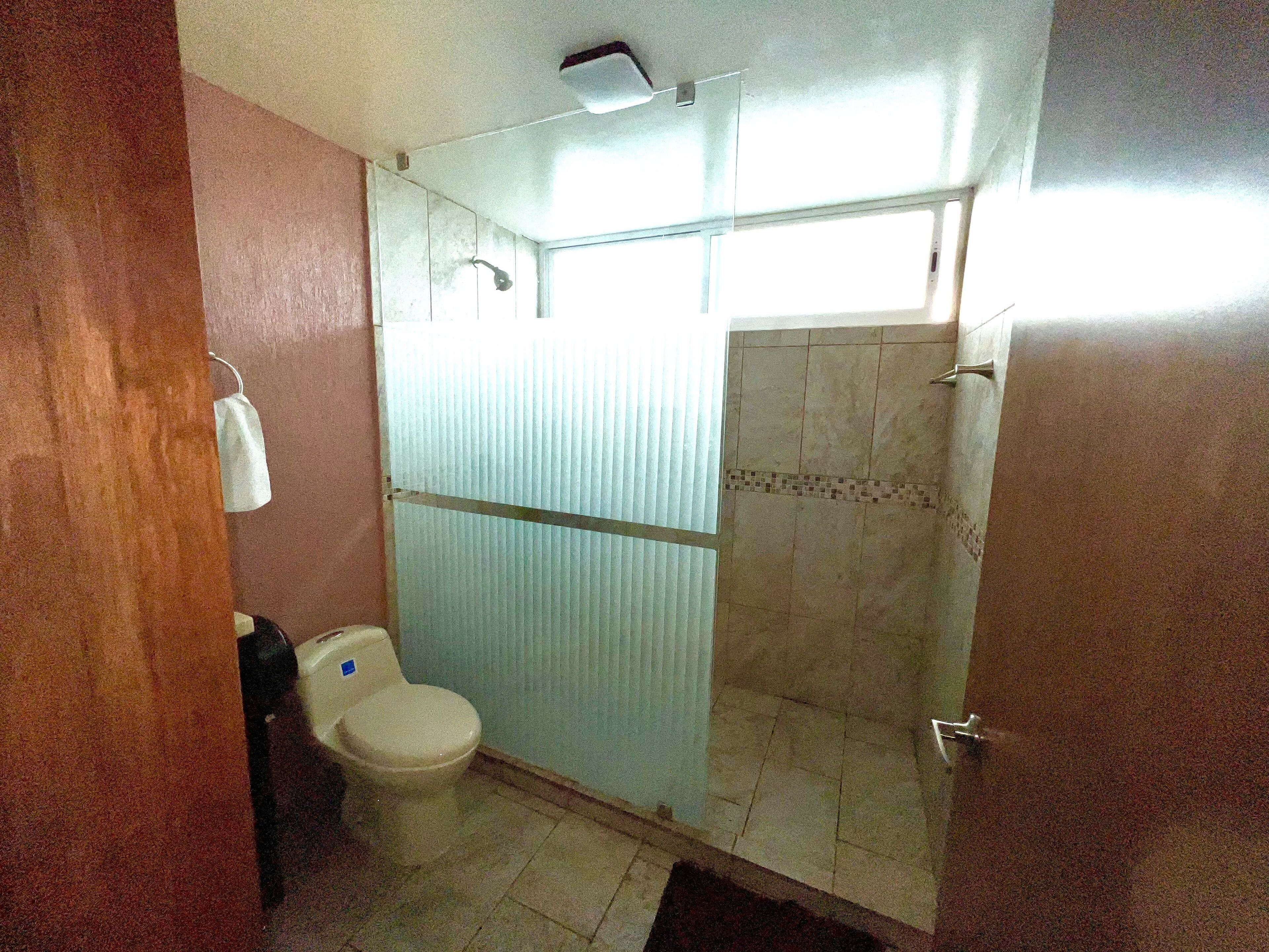 Un bagno con il water, uno spazio doccia e un asciugamano appeso al muro.