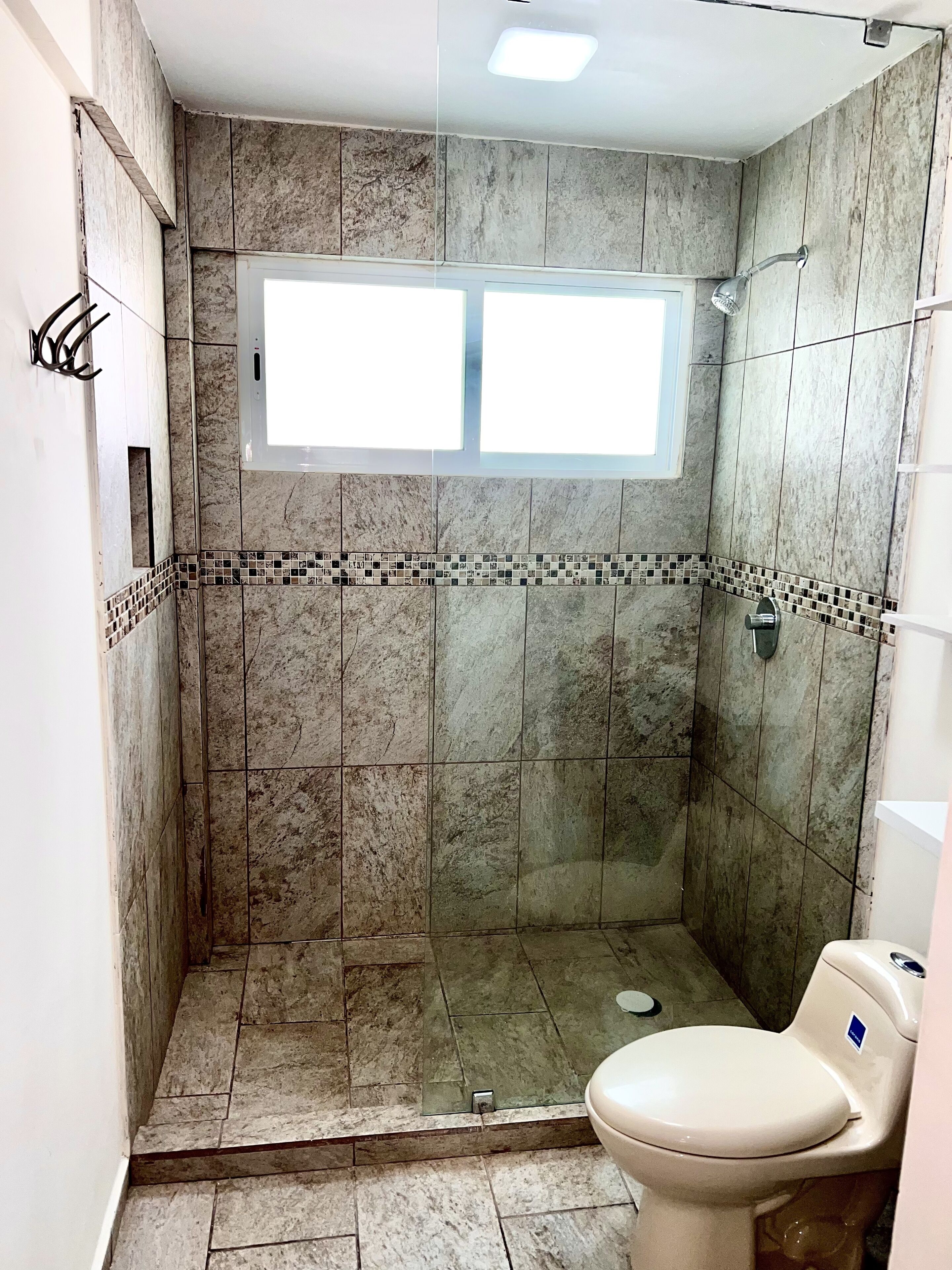 A shower stall with a window, a toilet, and tiled walls.
