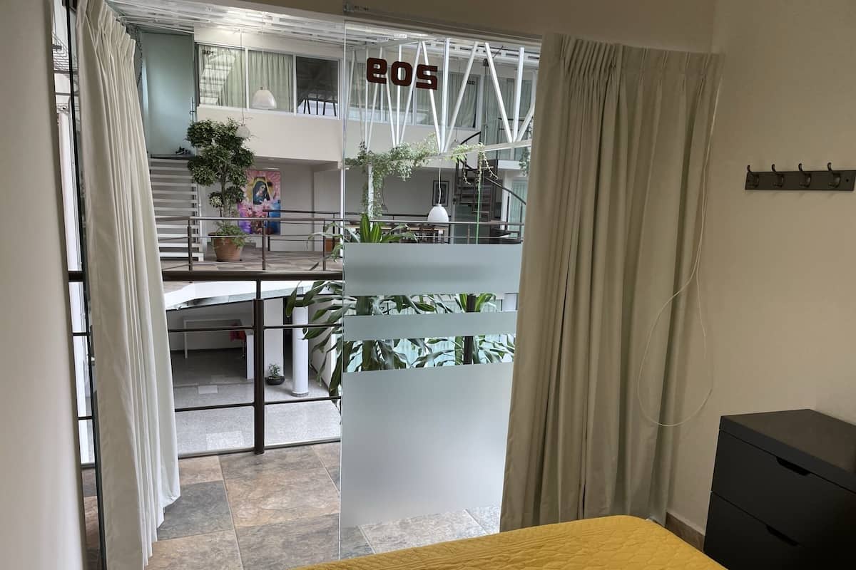 Une chambre d’hôtel avec un lit, un bureau et un balcon agrémenté de plantes.