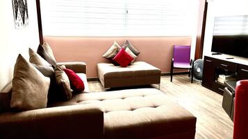 Una sala de estar con un sofá, un reposapiés y un televisor.