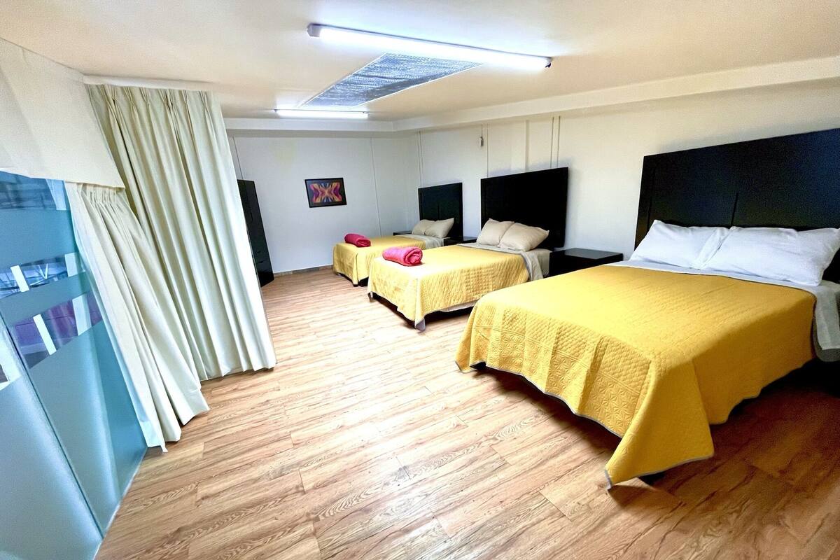 Une chambre d’hôtel avec deux lits, un plancher en bois, une grande fenêtre avec des rideaux et un luminaire au plafond.