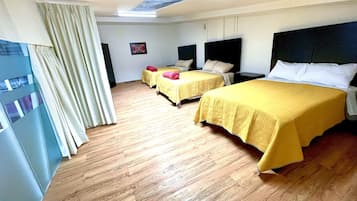 Habitación de hotel con dos camas, piso de madera, un ventanal grande con cortinas y una lámpara en el techo.