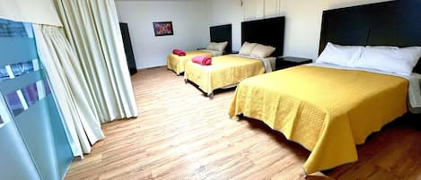 A hotel room with two beds, wooden flooring, a large window with curtains, and a ceiling light.