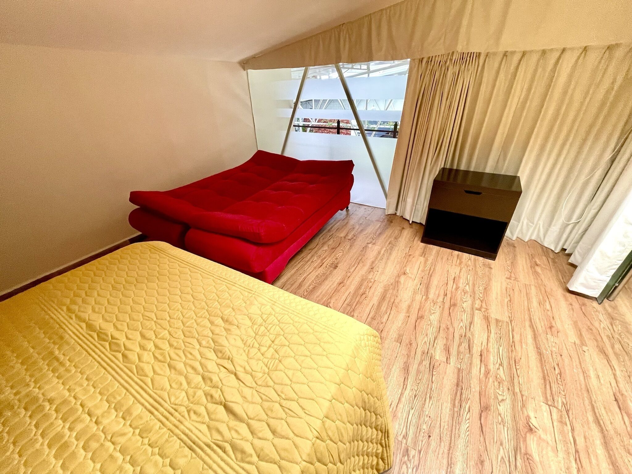 Una habitación con una cama, un sofá rojo, una mesita negra y una ventana con cortinas.