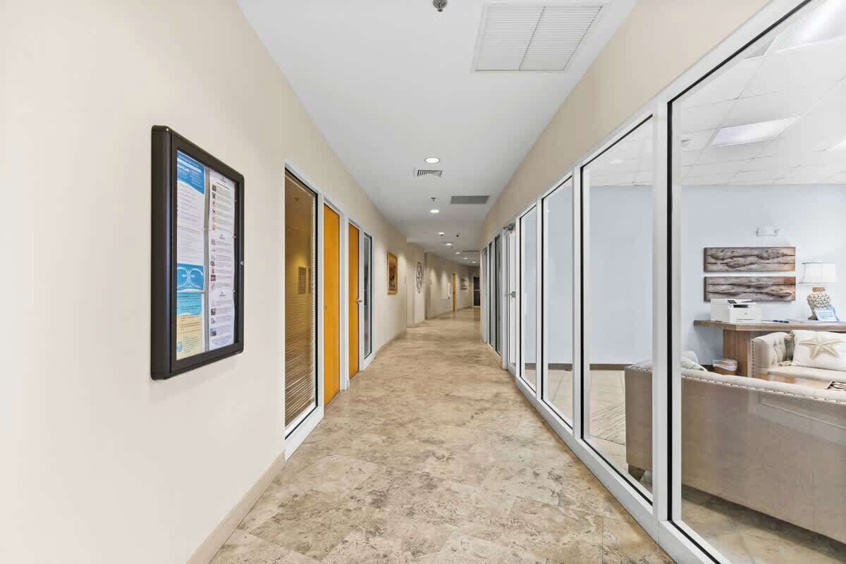 A corridor with glass doors, a bulletin board, and a reception area with a sofa and decorative items.