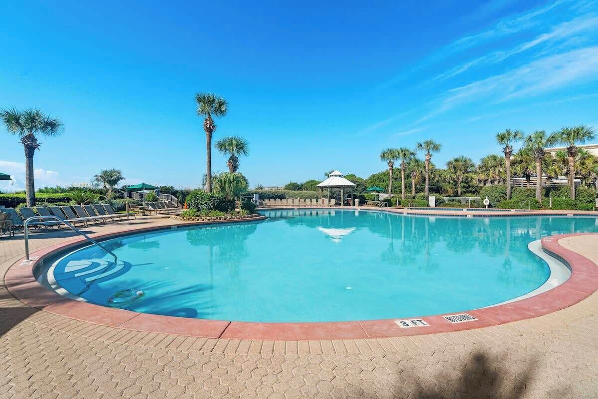 A swimming pool with a curved edge, surrounded by palm trees and lounge chairs.