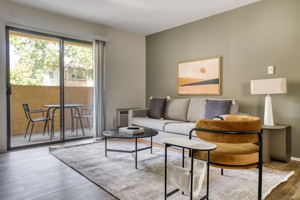 Relax in this stylish living room with a sofa, coffee table, and side table, plus a glass door leading to an outdoor seating area.