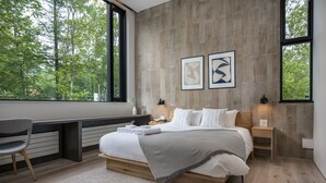 A modern bedroom with a large bed, a desk, and a view of trees through large windows. - Ryoun by H2 Life (Kutchan)