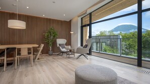 A modern interior with a wooden wall, a dining area, and a large window offering a mountain view. - Ryoun by H2 Life (Kutchan)