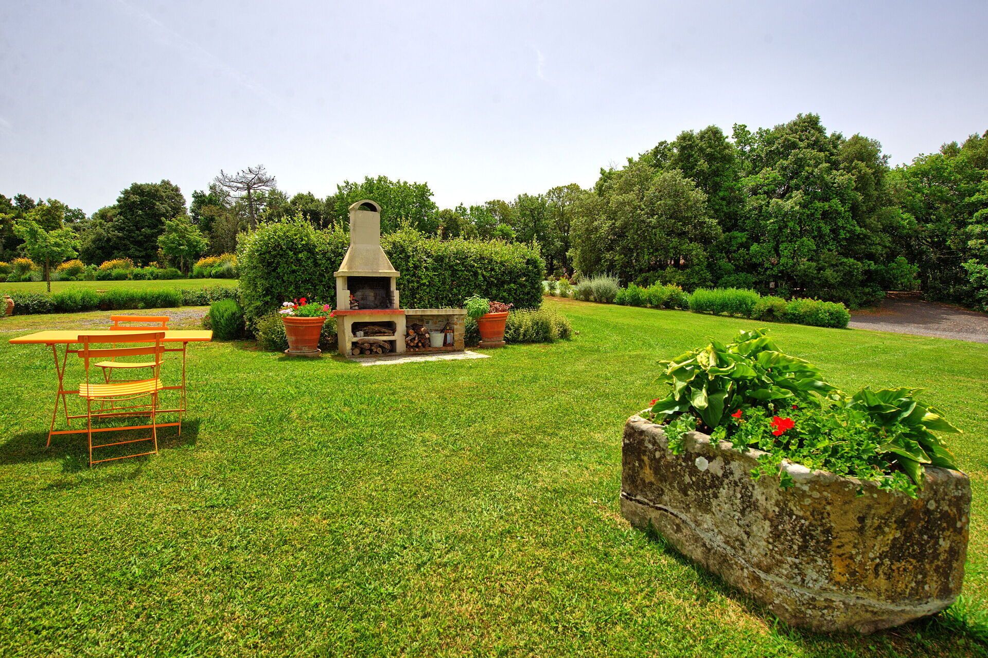 A garden with a stone barbecue, a wooden table with chairs, and a flower bed.