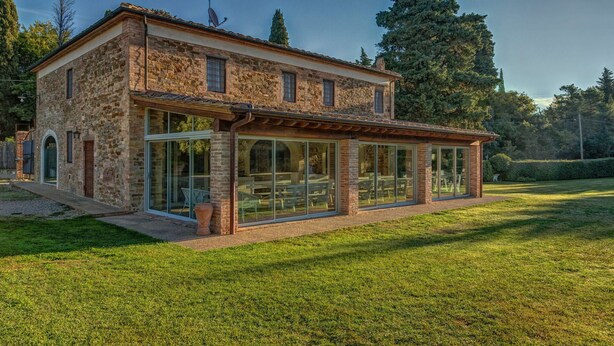 Une maison en pierre avec une extension en verre, une terrasse et une pelouse.
