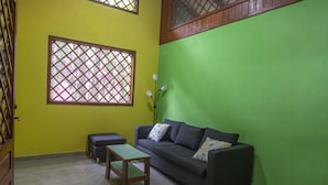 A room with a green wall, a black sofa with cushions, a wooden table, and a window with a lattice design.