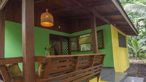 A wooden bench under a covered area with a woven light fixture, green walls, and a small window with a lattice design.