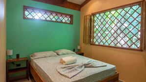 A bedroom with a bed, two nightstands, a window with a lattice design, and a view of greenery outside.