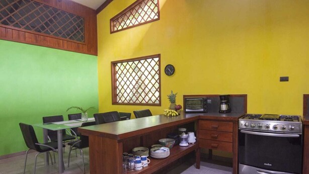 A kitchen with a dining area, a stove, a microwave, and a clock on the wall.
