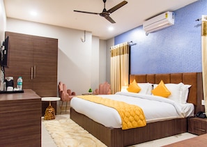 A modern hotel room with a large bed, a desk with a chair, a small table, and a ceiling fan.