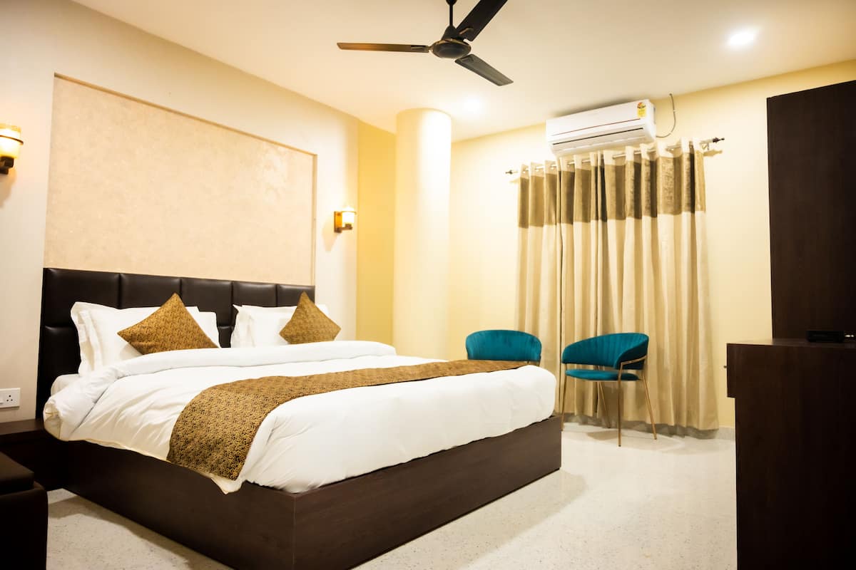Ein Hotelzimmer mit einem großen Bett, einem Deckenventilator, einer Klimaanlage, zwei Stühlen und einem Schreibtisch.