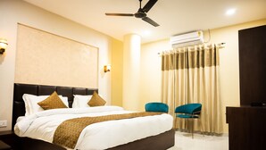 Habitación de hotel con una cama grande, ventilador de techo, equipo de aire acondicionado, dos sillas y un escritorio.