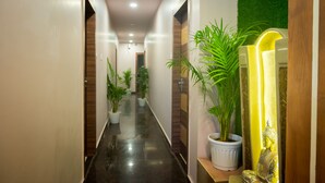 Un pasillo con plantas en macetas, una estatua de Buda y un espejo que refleja la luz.
