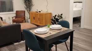 Un'area pranzo con un tavolo apparecchiato per due, un armadietto in legno, un televisore a parete e una finestra con persiane.