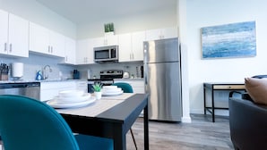 Una cucina moderna con mobili bianchi, elettrodomestici in acciaio inossidabile e un'area pranzo con sedie color acquamarina.
