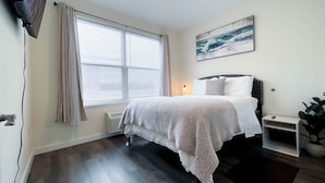 Una camera da letto con un letto, una finestra con tende, un quadro appeso al muro e una pianta.