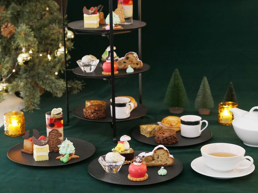 Een etagère met diverse gebakjes en een theepot op een tafel, omringd door kaarsen en een kerstboom.
