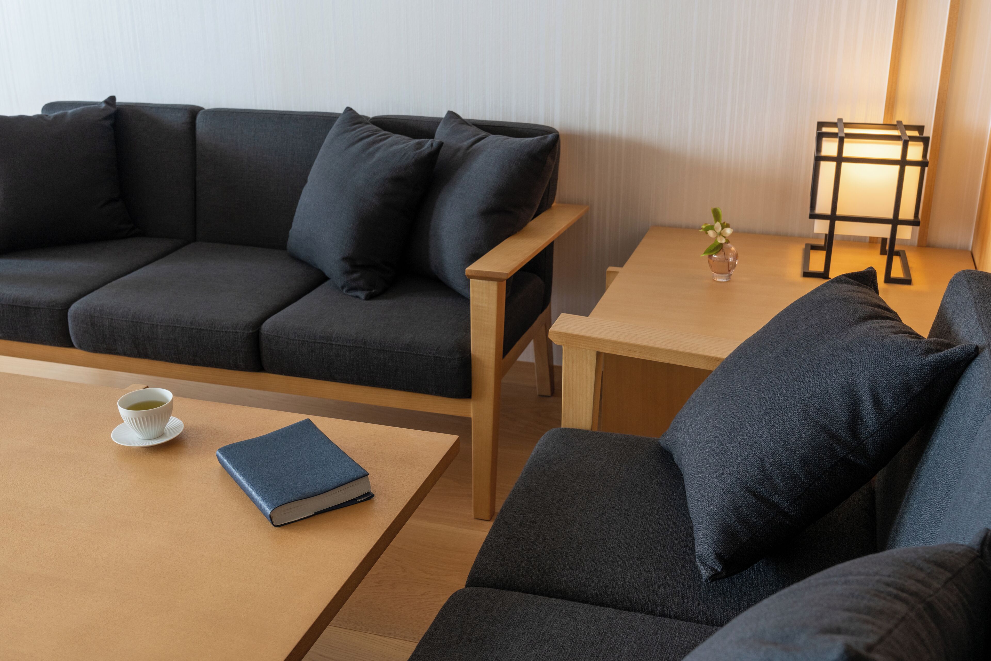 Una sala moderna con un sofá gris oscuro, una mesa de centro de madera y una mesita auxiliar con una lámpara y un jarrón de flores.