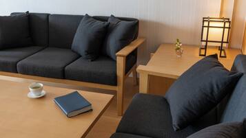 Una sala moderna con un sofá gris oscuro, una mesa de centro de madera y una mesita auxiliar con una lámpara y un jarrón de flores.