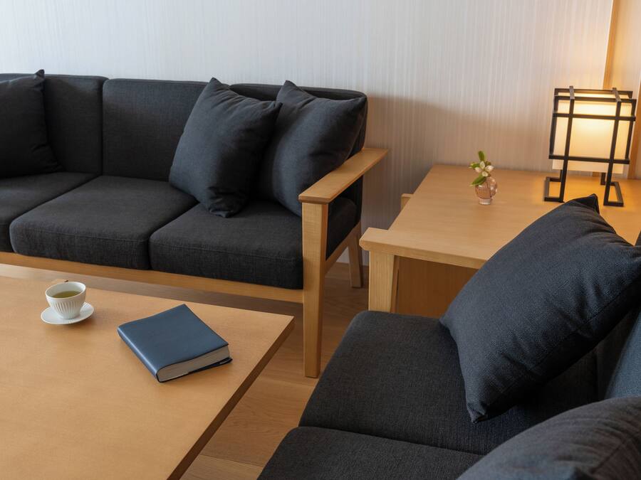 Una sala moderna con un sofá gris oscuro, una mesa de centro de madera y una mesita auxiliar con una lámpara y un jarrón de flores.