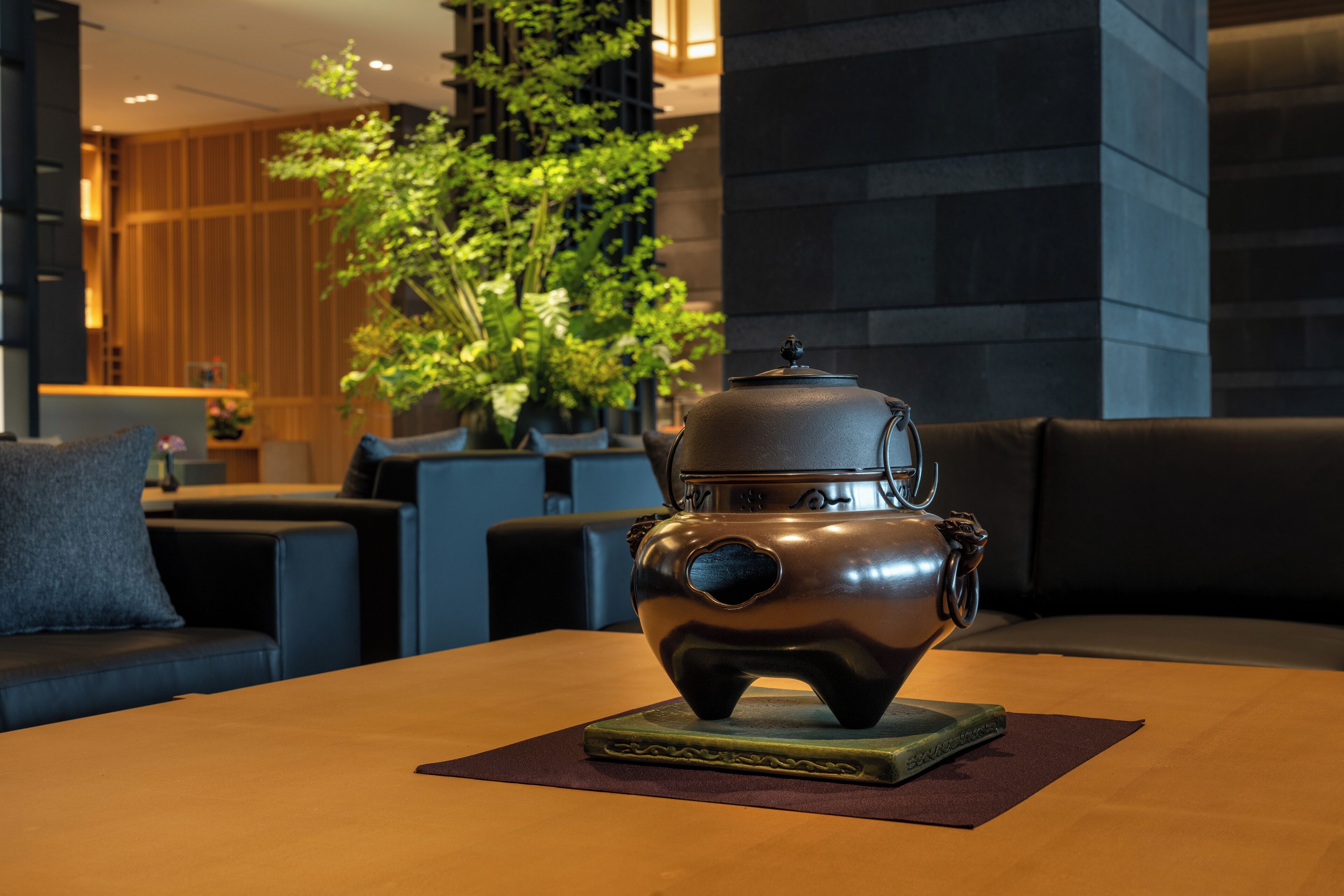 A traditional tea pot on a table in a modern room with a sofa and potted plants.