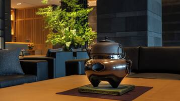 A traditional tea pot on a table in a modern room with a sofa and potted plants.