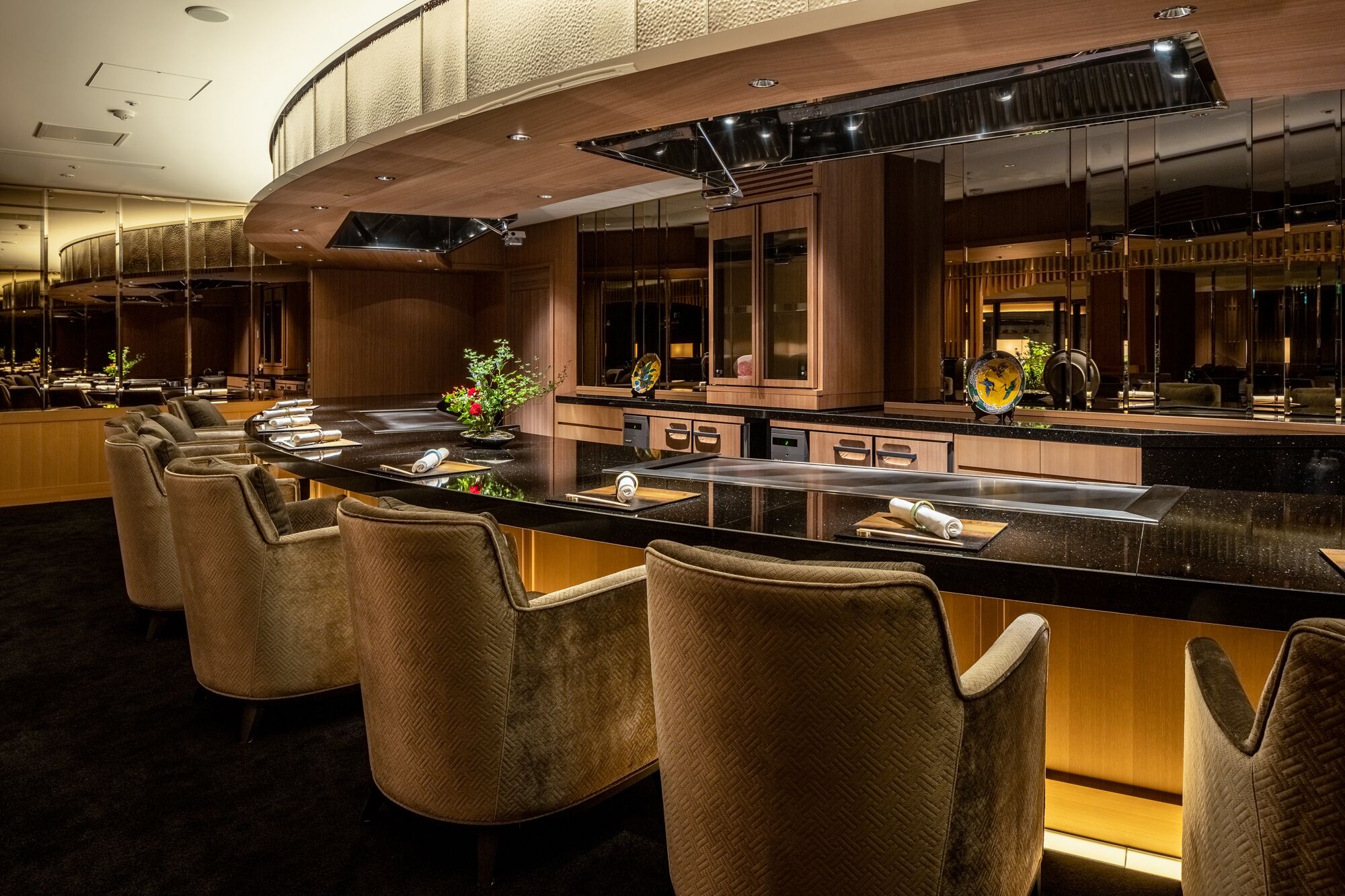 A modern bar area with a curved counter, multiple seating options, and a large mirror.