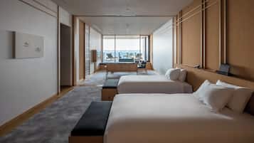 A modern hotel room with two beds, a seating area with a view, and a large window.