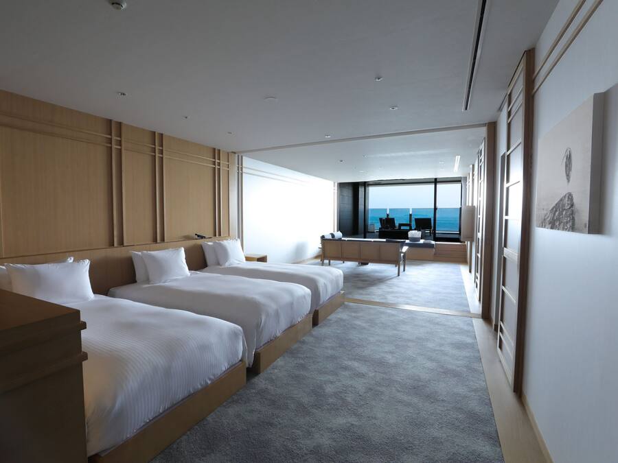 A modern hotel room with a large bed, a desk, and a view of the ocean.