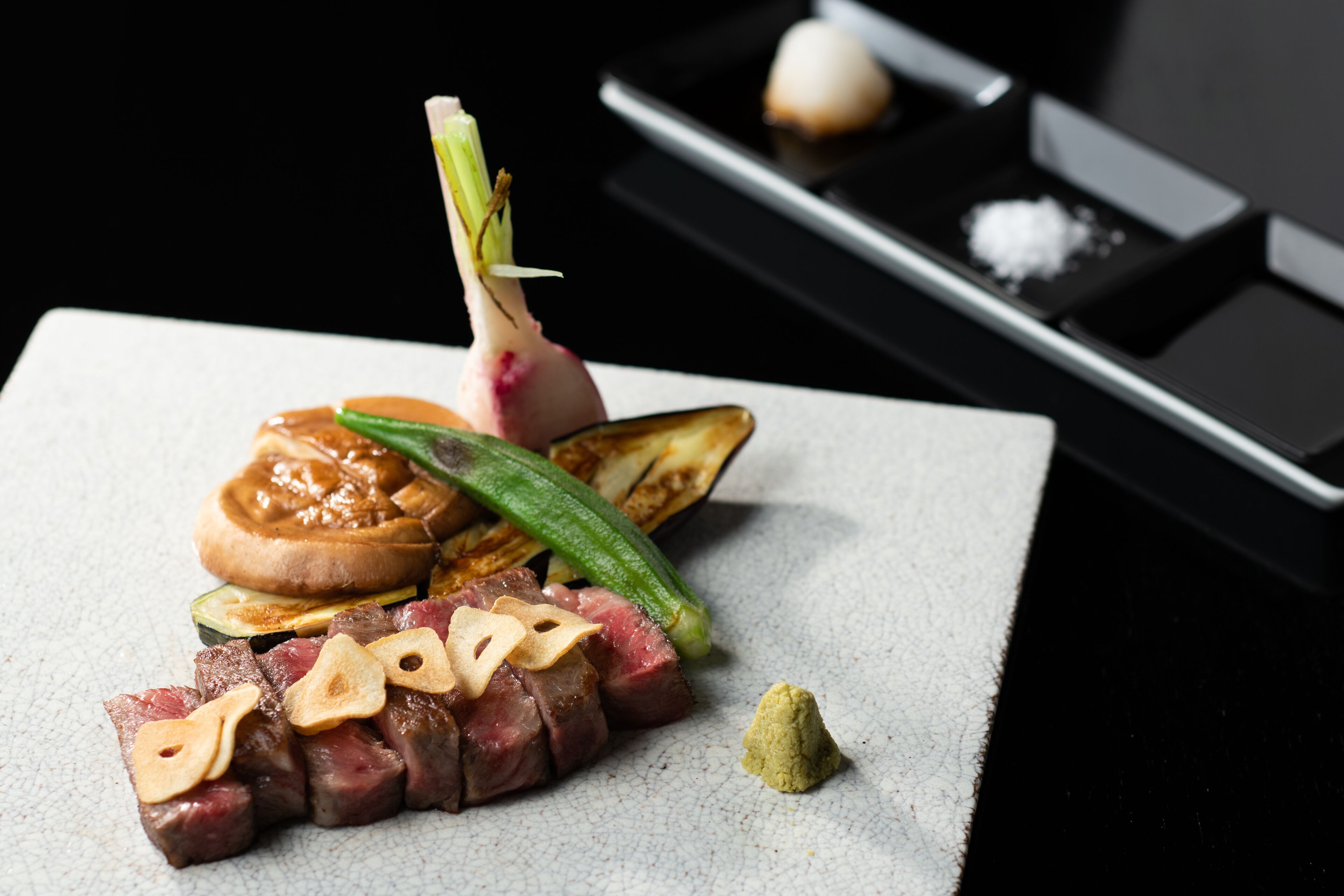 Een bord eten met diverse ingrediënten, zoals vlees, groenten en een klein schaaltje zout.