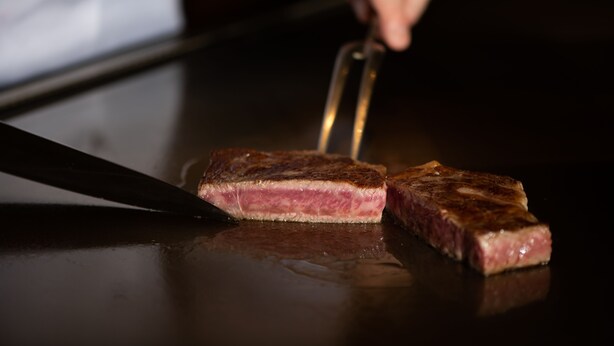 Bife sendo cortado com uma faca em uma superfície espelhada.