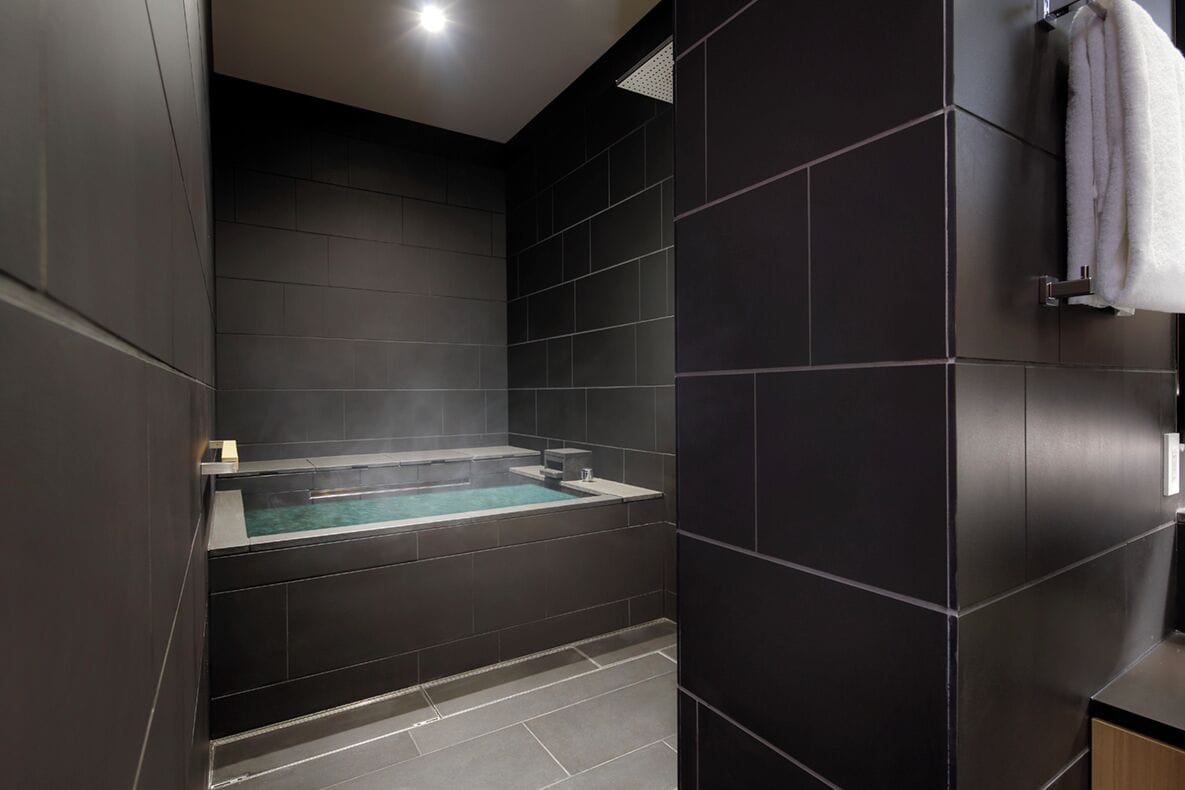A modern bathroom with a built-in jacuzzi, dark tiled walls, and a towel rack.