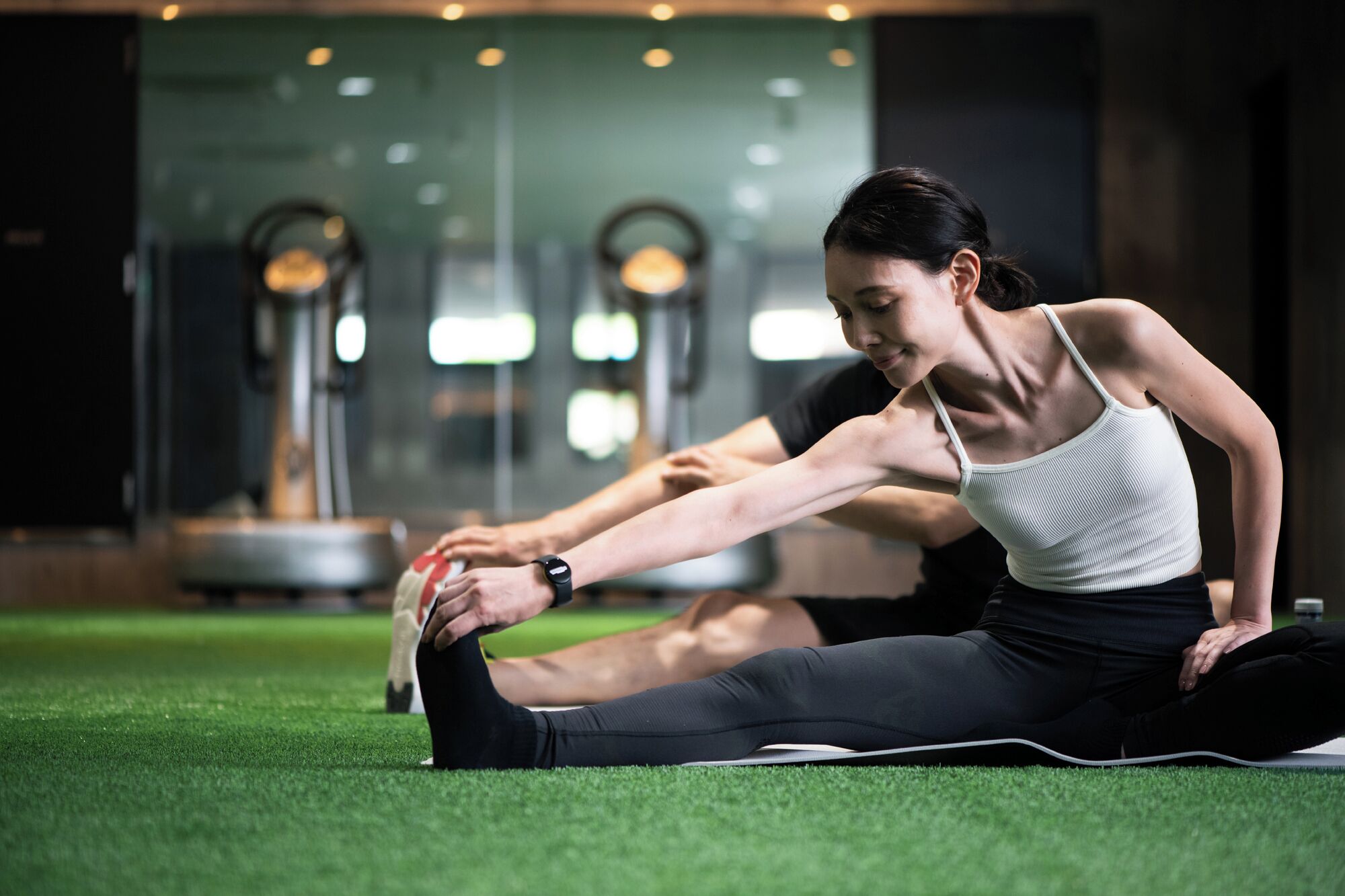 A person stretching on a mat in a gym with exercise equipment in the background.