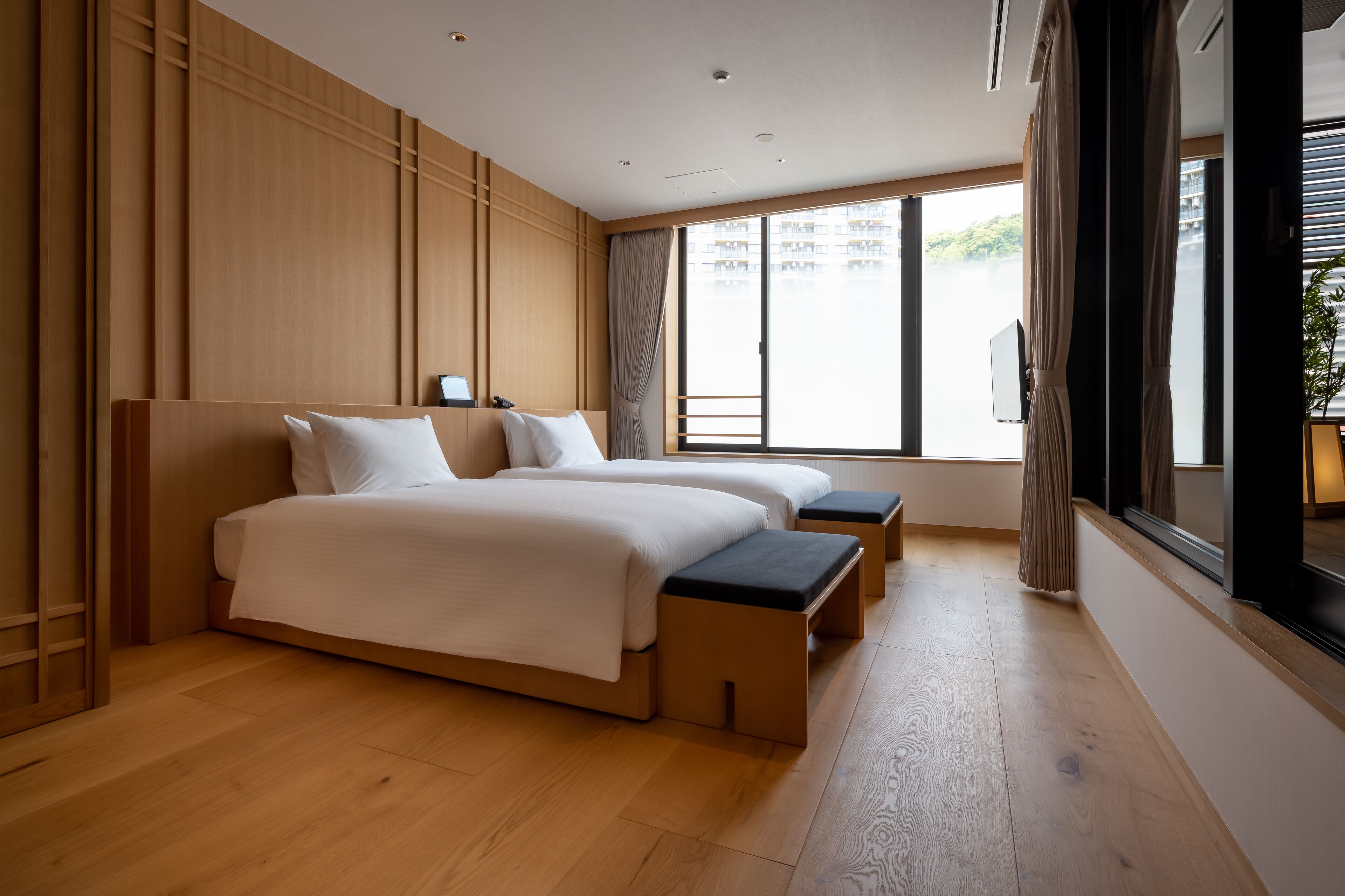 A modern hotel room with a large bed, a smaller bed, and a bench.