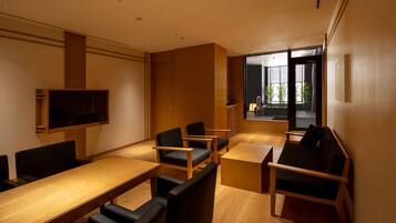 A modern meeting room with a long table, several chairs, a television, and a large window offering a view of the outdoors.