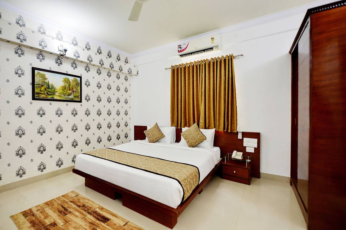 A bedroom with a bed, a nightstand, a wooden wardrobe, a wall-mounted air conditioner, and patterned wallpaper.