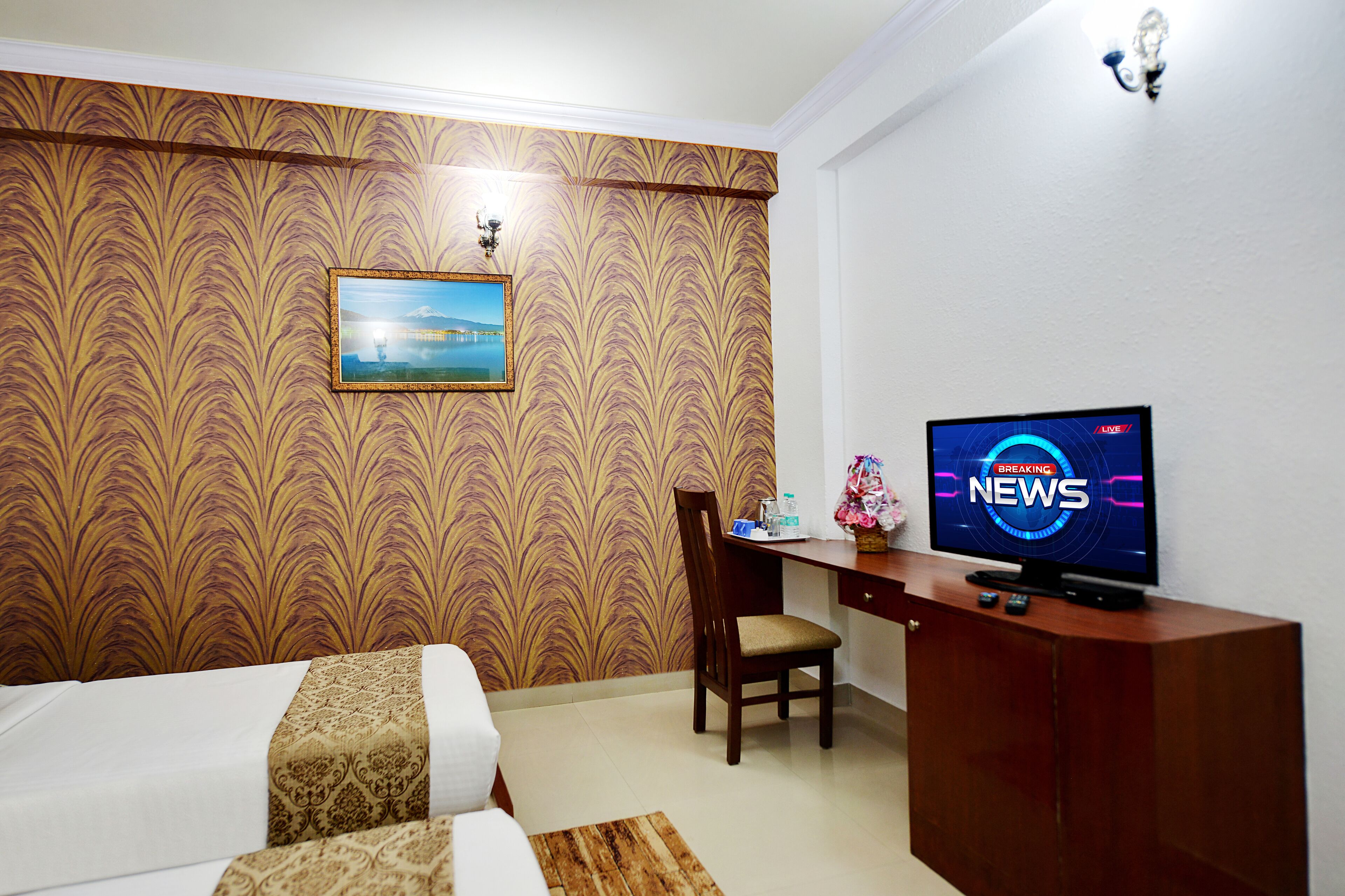 A hotel room with a bed, a desk, a television displaying 'Breaking News', and a patterned wallpaper.